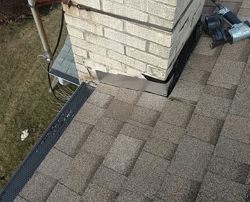 Close-up of shingles and a chimney on a roof with visible tools, including a nail gun, highlighting the meticulous efforts in commercial roofing.