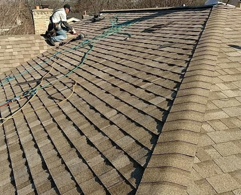 Workers on a roof installing shingles under clear skies, with tools and materials spread around them, showcasing the efficiency of a skilled roofing company.