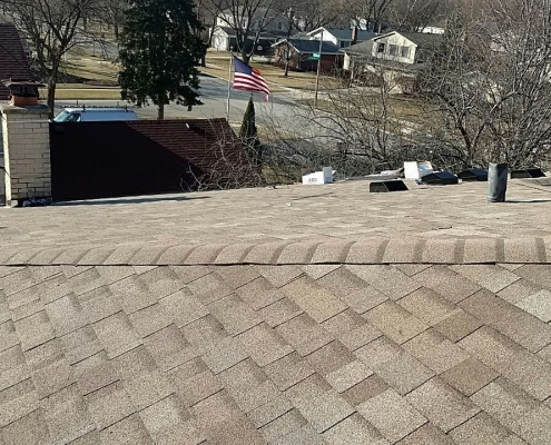 A view of a residential neighborhood from the rooftop reveals asphalt shingles and roof vents. An American flag flutters in the distance, among houses and bare trees—a scene that underscores the work of a skilled roofing contractor dedicated to pristine roof installations.