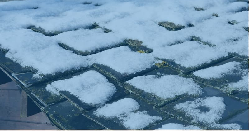 The snow-covered roof, showing visible wear and tear, hints at the relentless Illinois winters. The Revived Exteriors logo sits in the bottom corner, symbolizing a commitment to durable roofing materials and thermal efficiency.